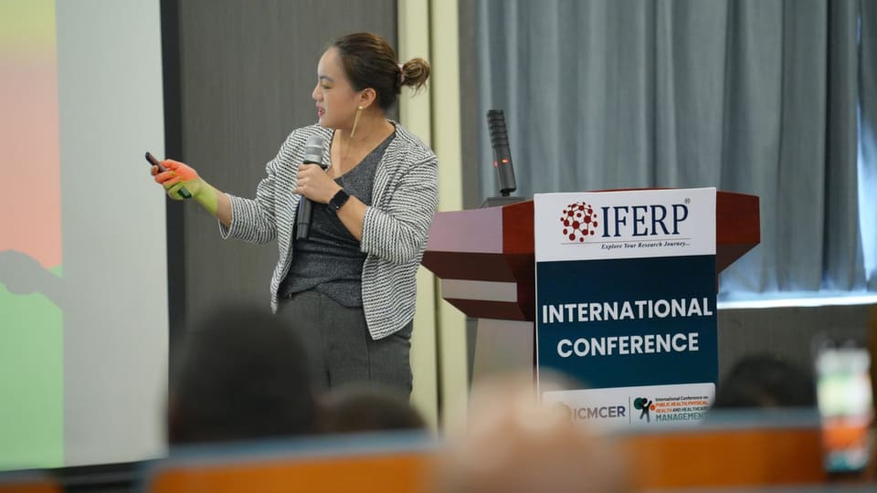 A researcher presenting from the podium with slides projected beside her at an IFERP conference